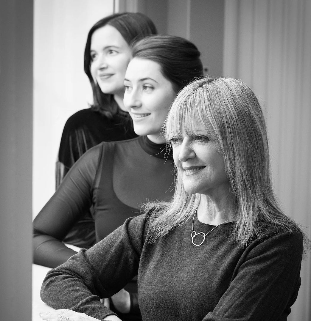 A black and white photo of three women in foreground, midground, and background looking away from the camera.